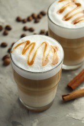 Photo of Tasty latte macchiato in glasses, coffee beans and cinnamon on grey table, closeup