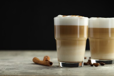 Photo of Tasty latte macchiato in glasses, coffee beans and cinnamon on grey table, closeup. Space for text