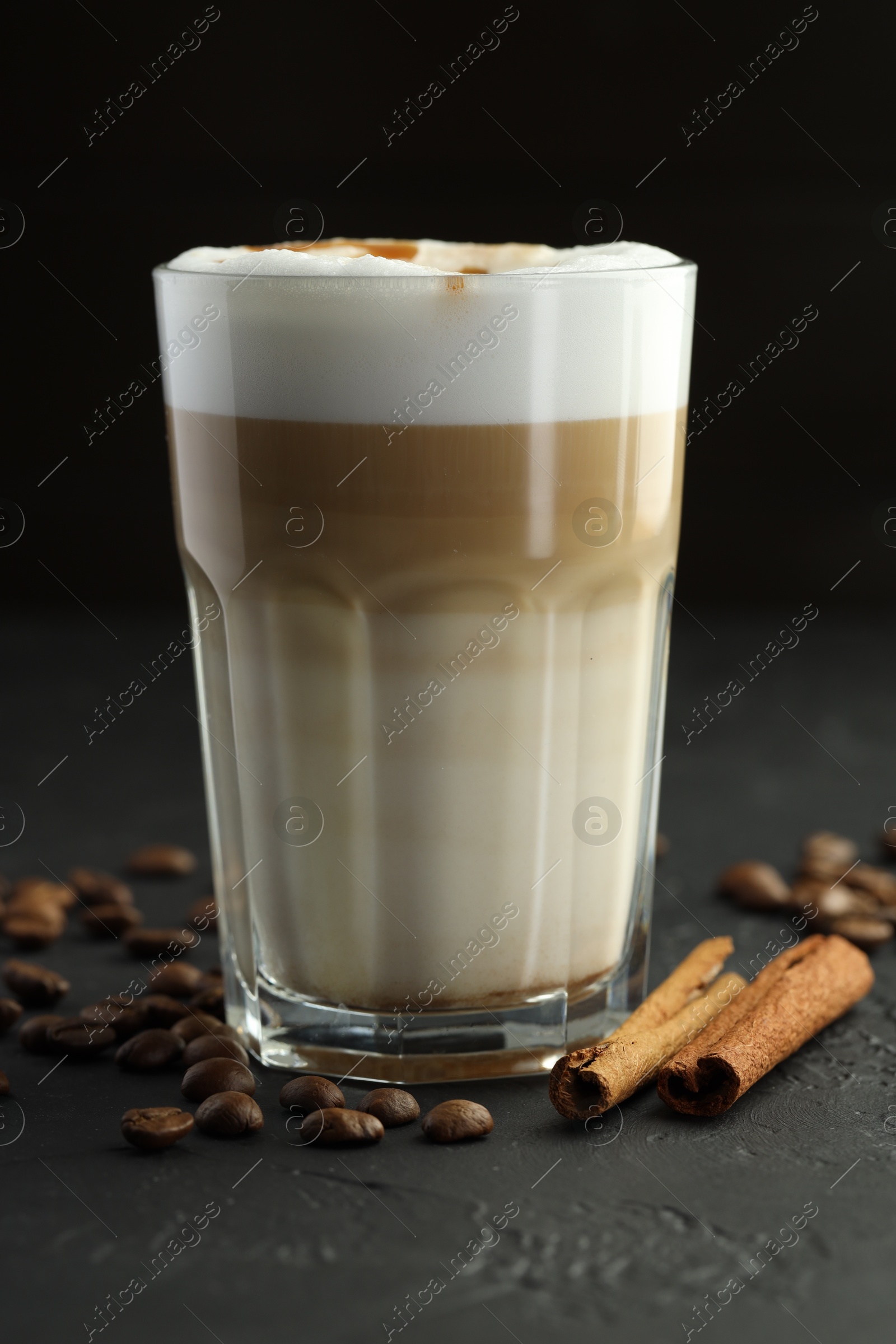 Photo of Tasty latte macchiato in glass, coffee beans and cinnamon on black table, closeup