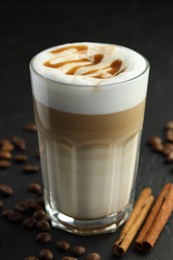 Photo of Tasty latte macchiato in glass, coffee beans and cinnamon on black table, closeup