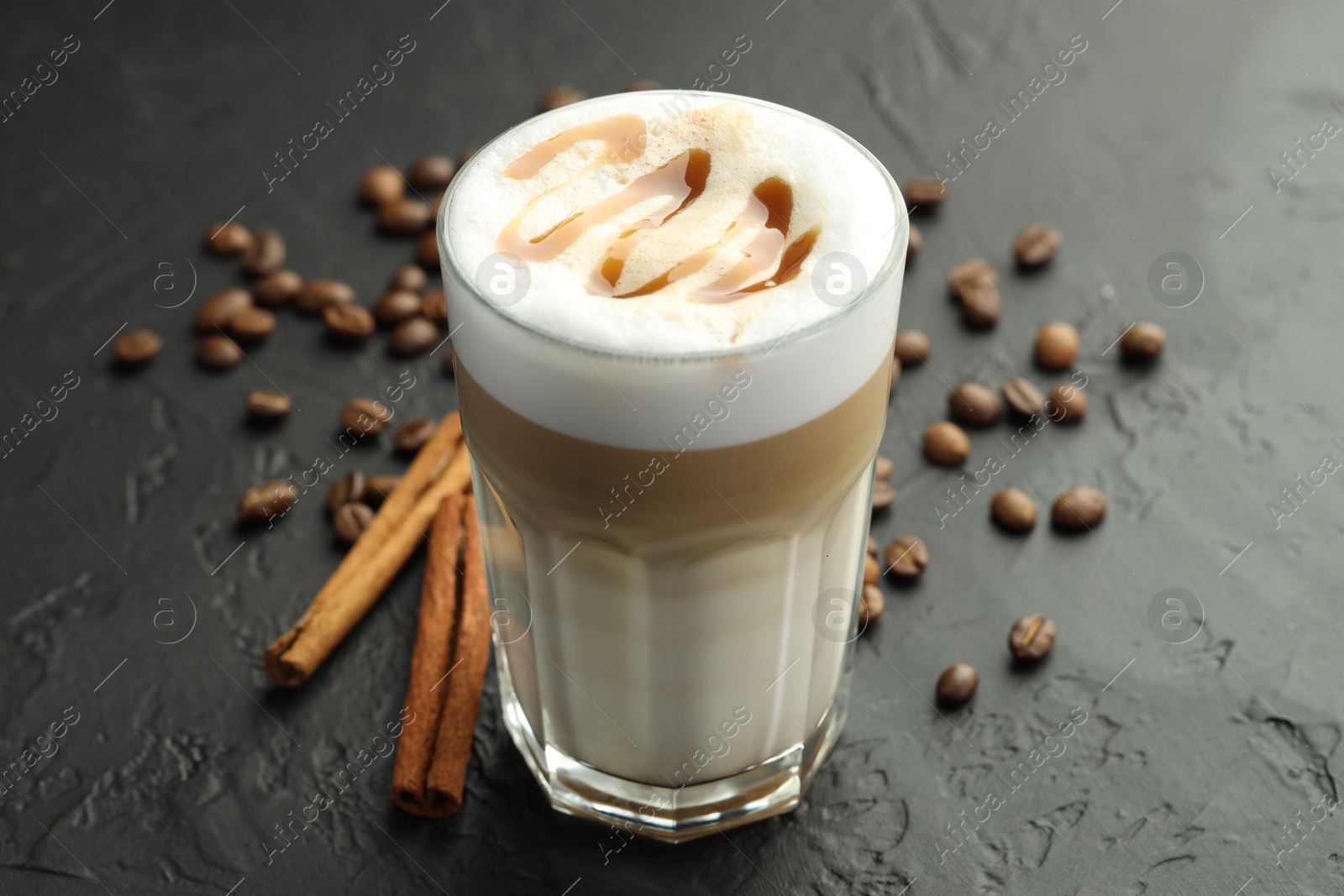 Photo of Tasty latte macchiato in glass, coffee beans and cinnamon on black table, closeup