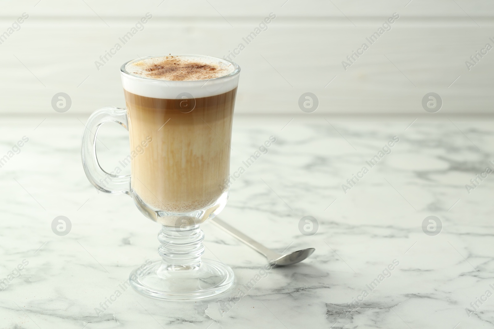 Photo of Tasty latte macchiato in glass cup on white marble table, closeup. Space for text