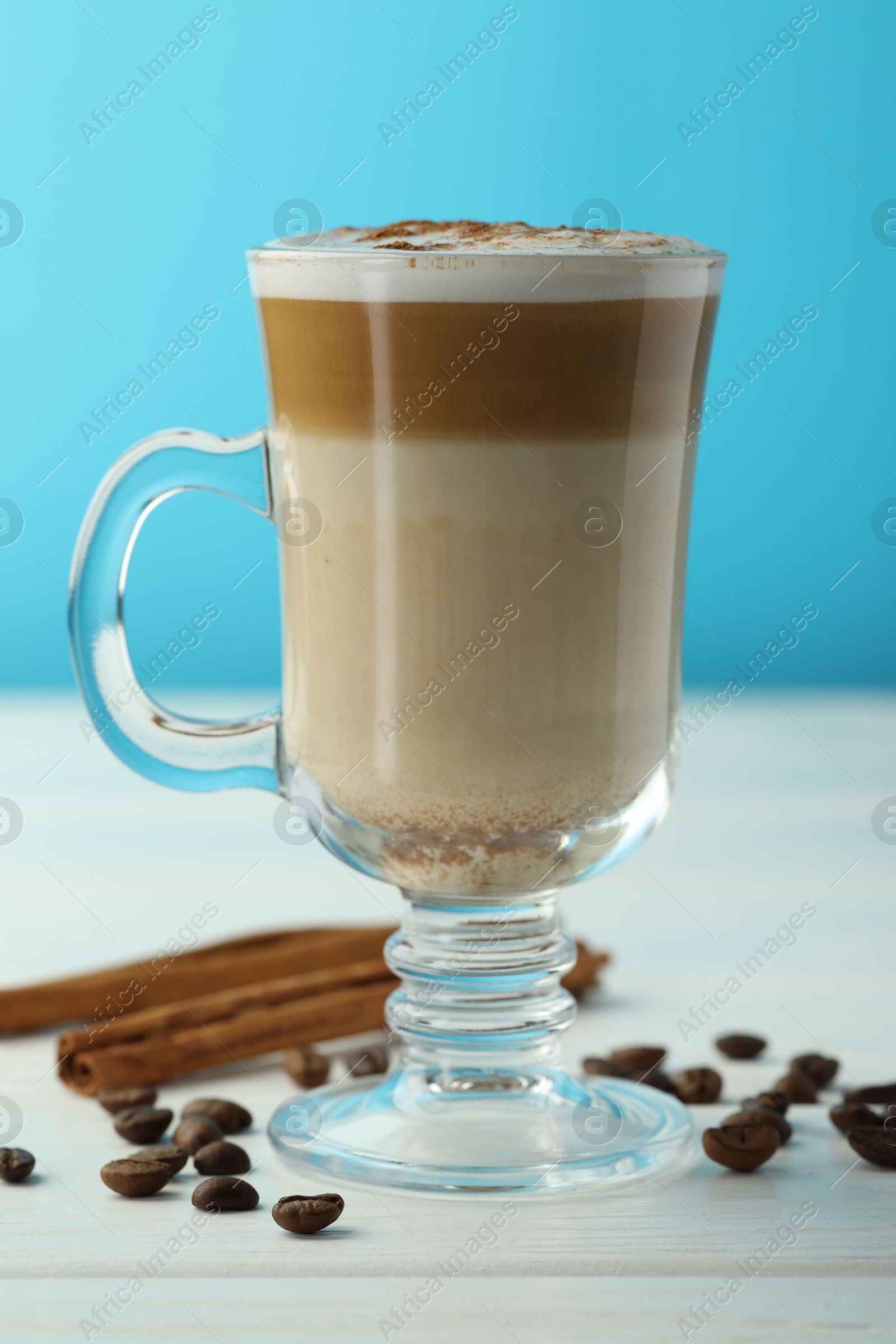 Photo of Tasty latte macchiato in glass cup, coffee beans and cinnamon on white wooden table, closeup