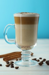 Photo of Tasty latte macchiato in glass cup, coffee beans and cinnamon on white wooden table, closeup