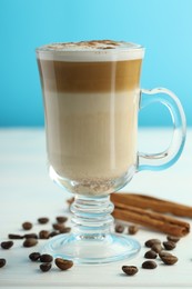 Photo of Tasty latte macchiato in glass cup, coffee beans and cinnamon on white wooden table, closeup