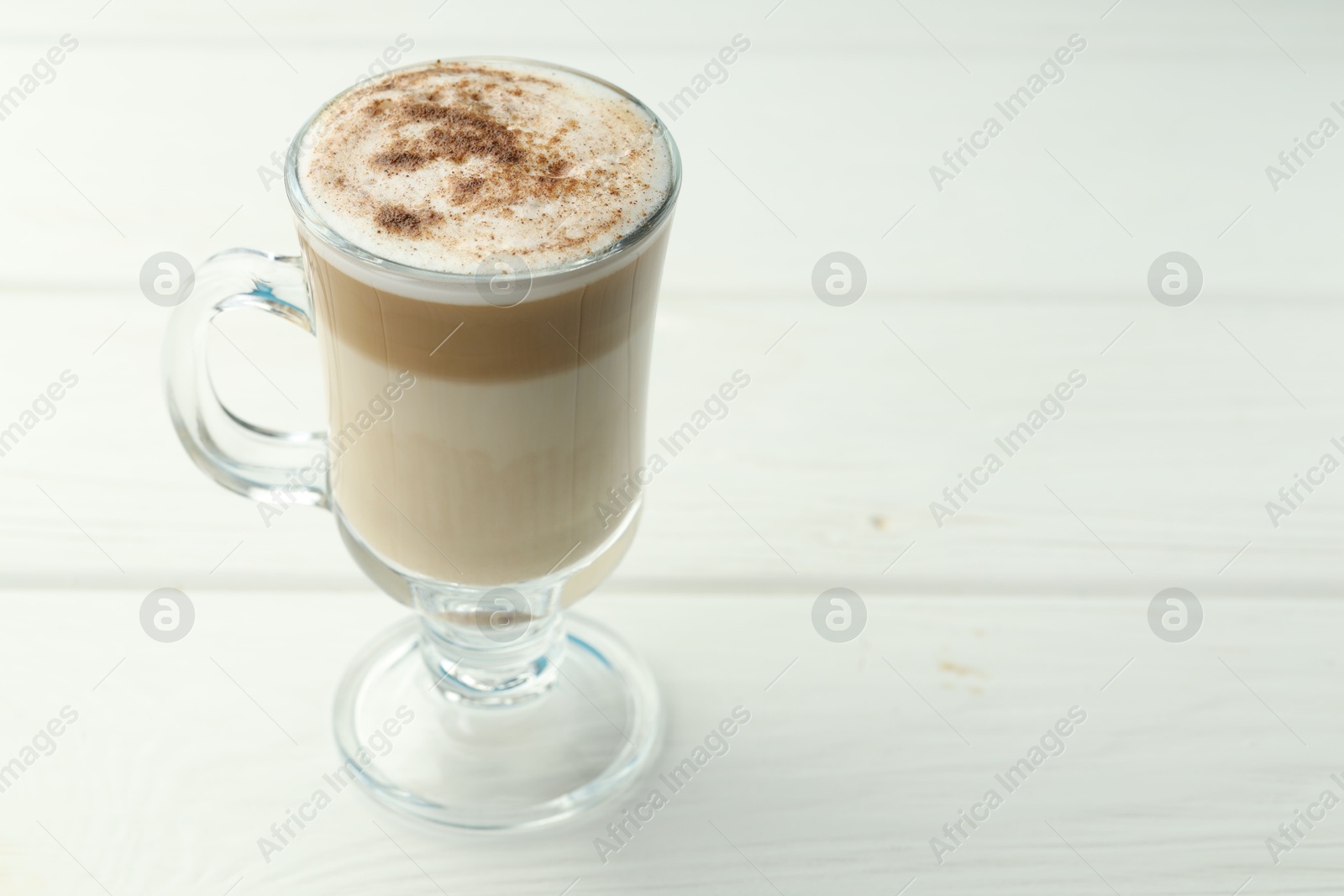 Photo of Tasty latte macchiato in glass cup on white wooden table, closeup. Space for text