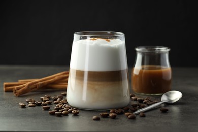 Photo of Tasty latte macchiato in glass, coffee beans and cinnamon on grey table, closeup