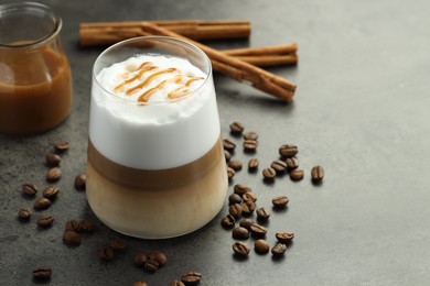 Photo of Tasty latte macchiato in glass, coffee beans and cinnamon on grey table, closeup. Space for text