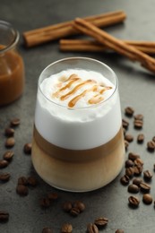 Photo of Tasty latte macchiato in glass, coffee beans and cinnamon on grey table, closeup