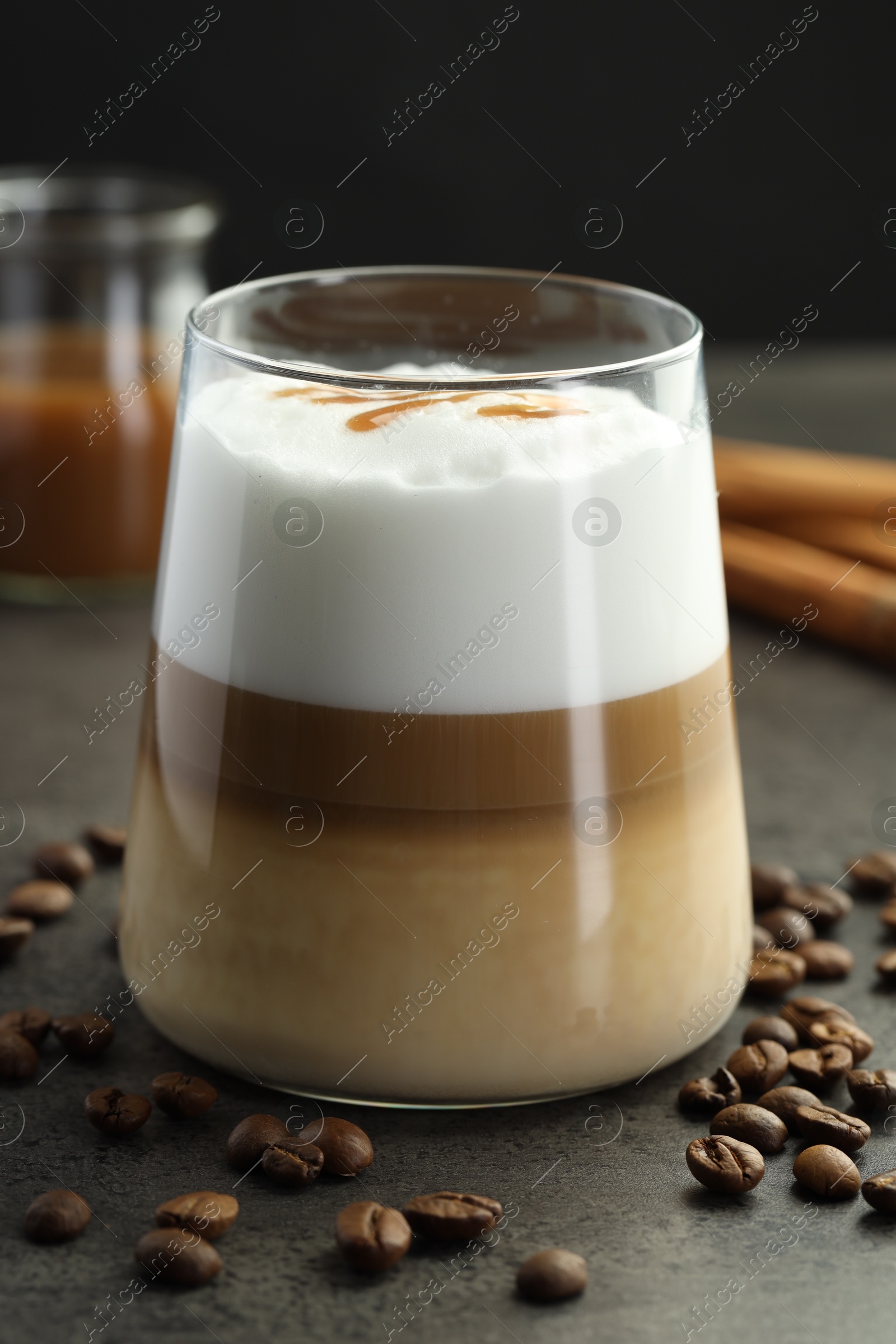 Photo of Tasty latte macchiato in glass, coffee beans and cinnamon on grey table, closeup