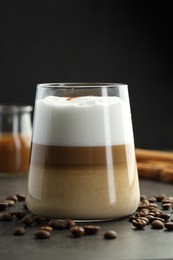 Photo of Tasty latte macchiato in glass, coffee beans and cinnamon on grey table, closeup