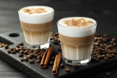 Photo of Tasty latte macchiato in glasses, coffee beans and cinnamon on black wooden table, closeup