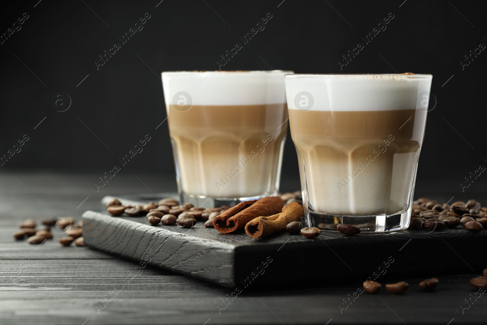 Photo of Tasty latte macchiato in glasses, coffee beans and cinnamon on black wooden table, closeup