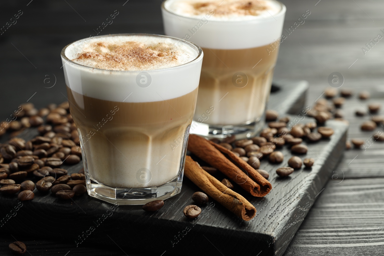 Photo of Tasty latte macchiato in glasses, coffee beans and cinnamon on black wooden table, closeup