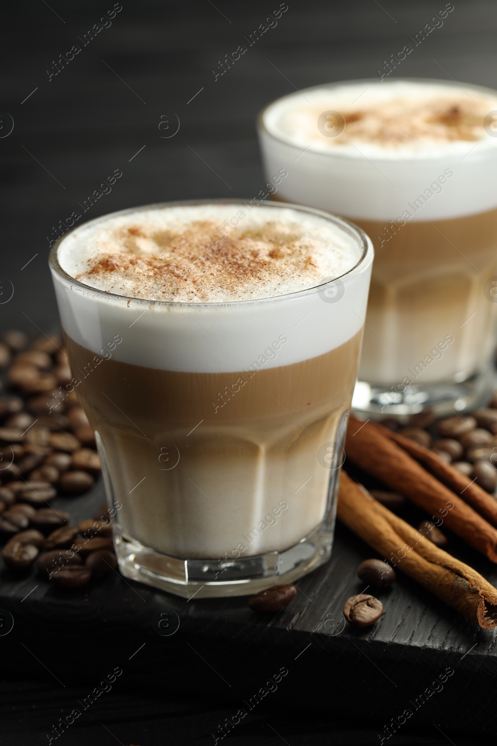 Photo of Tasty latte macchiato in glasses, coffee beans and cinnamon on black wooden table, closeup