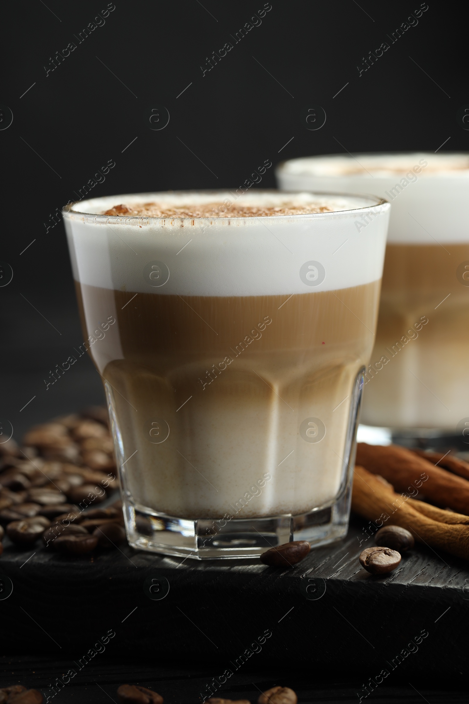 Photo of Tasty latte macchiato in glasses, coffee beans and cinnamon on black wooden table, closeup