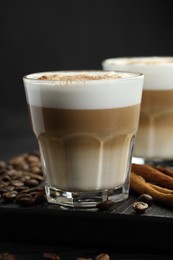 Photo of Tasty latte macchiato in glasses, coffee beans and cinnamon on black wooden table, closeup