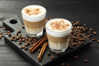 Photo of Tasty latte macchiato in glasses, coffee beans and cinnamon on black wooden table, closeup