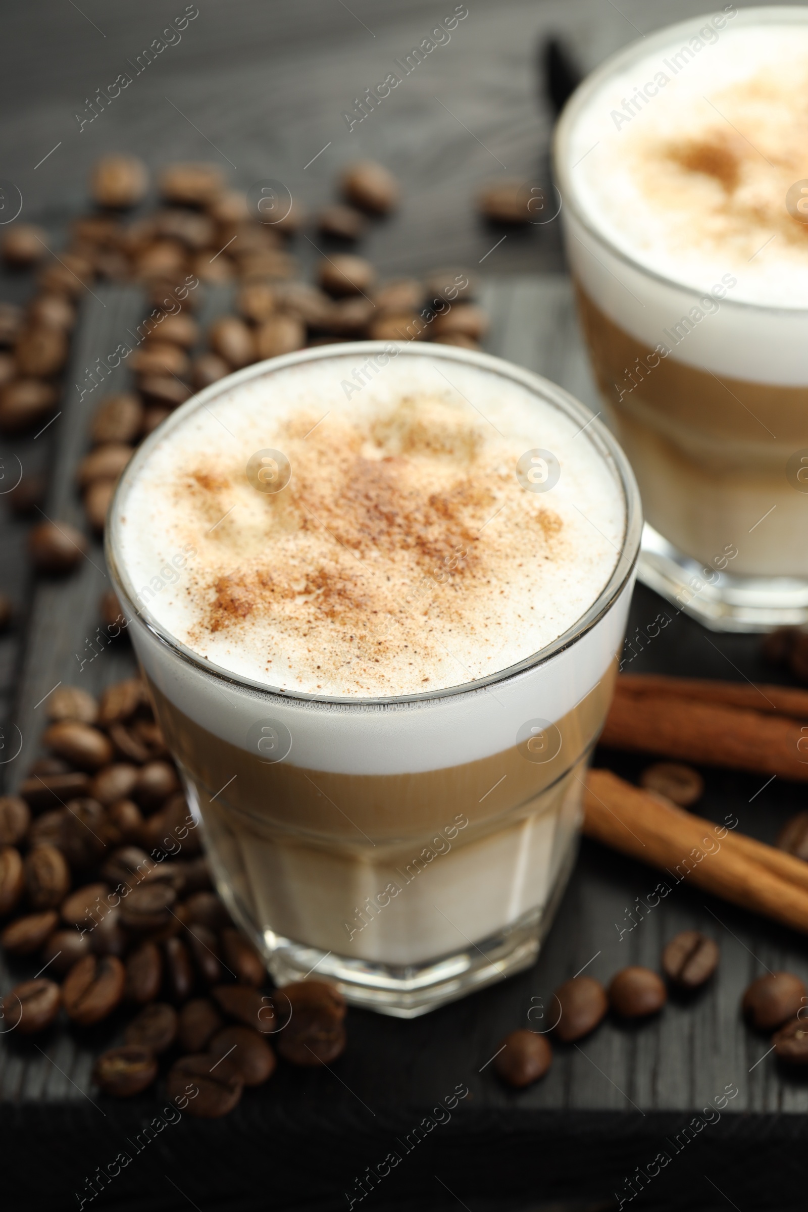 Photo of Tasty latte macchiato in glasses, coffee beans and cinnamon on black wooden table, closeup