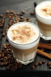 Photo of Tasty latte macchiato in glasses, coffee beans and cinnamon on black wooden table, closeup