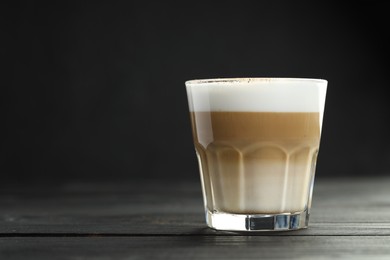 Photo of Tasty latte macchiato in glass on black wooden table, closeup. Space for text