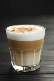 Photo of Tasty latte macchiato in glass on black wooden table, closeup