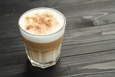 Photo of Tasty latte macchiato in glass on black wooden table, closeup. Space for text