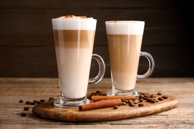 Photo of Tasty latte macchiato in glass cups, coffee beans and cinnamon on wooden table, closeup