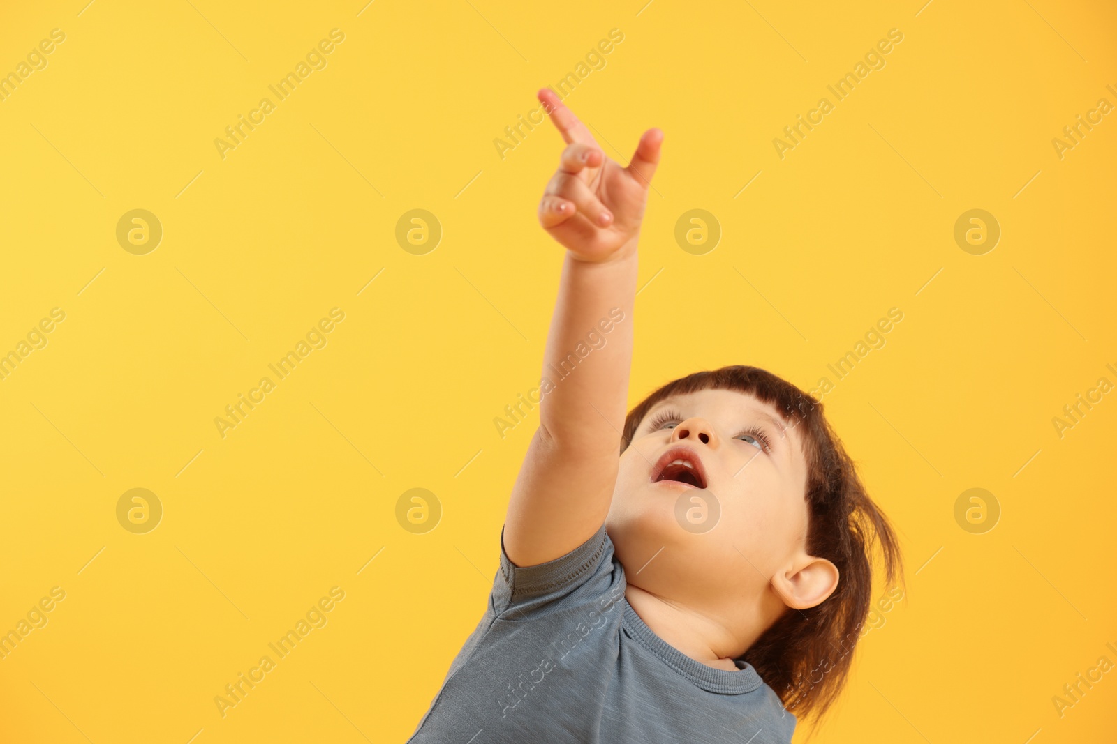 Photo of Little boy pointing upwards on yellow background. Space for text