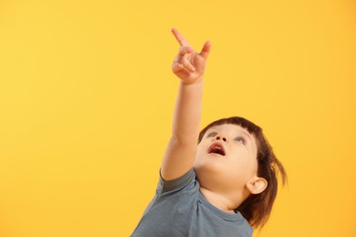 Photo of Little boy pointing upwards on yellow background. Space for text