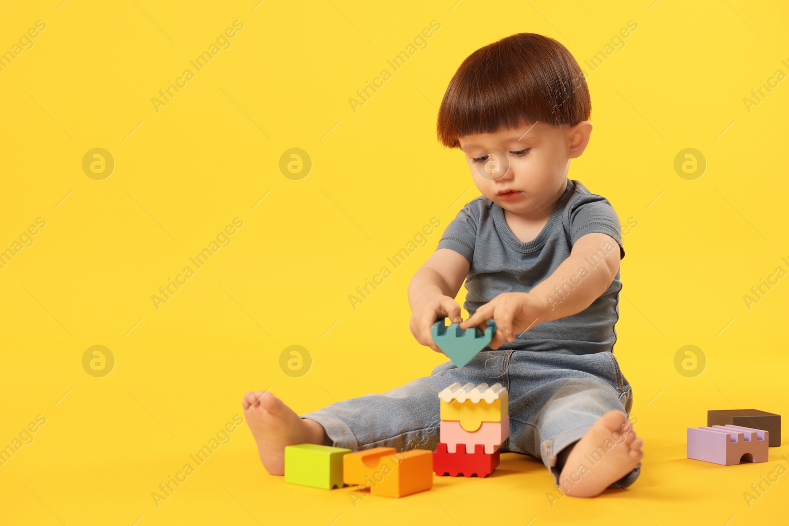 Photo of Cute little boy playing on yellow background. Space for text