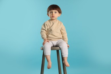 Photo of Cute little boy sitting on stool against light blue background