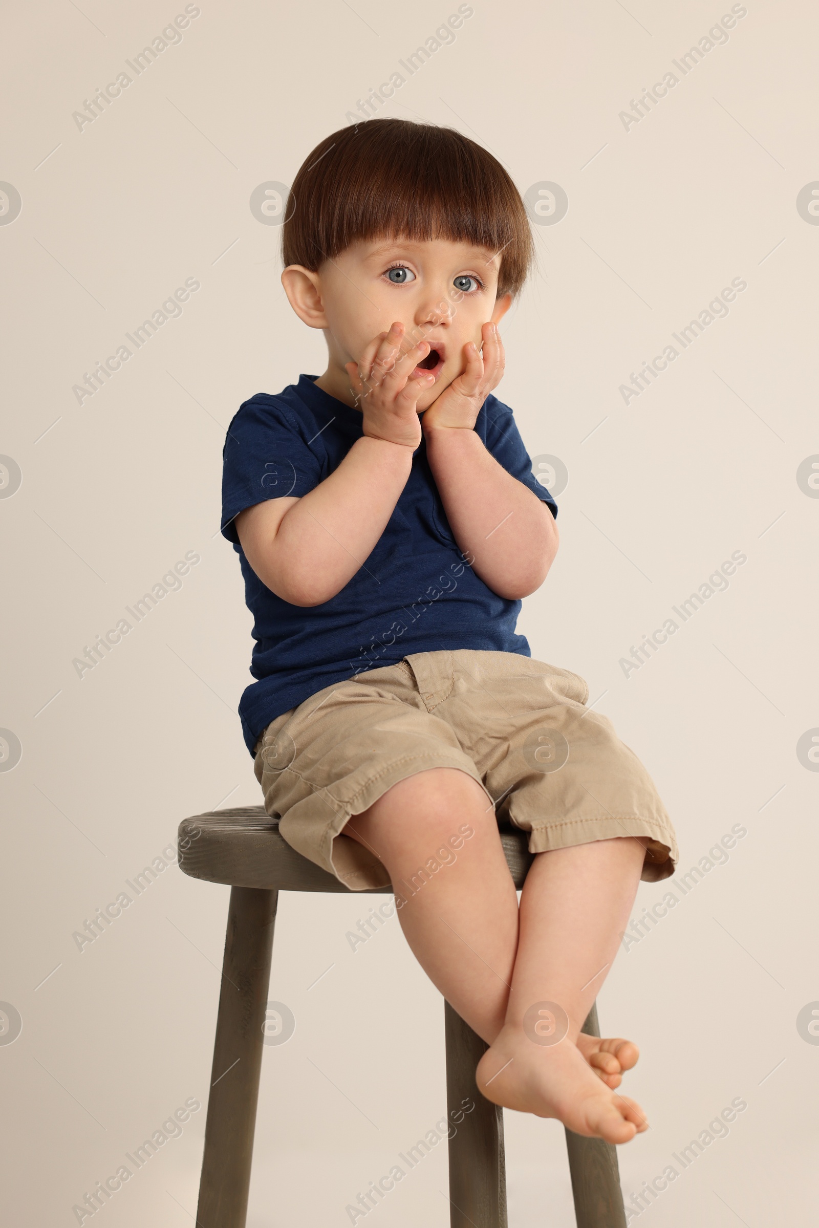 Photo of Emotional little boy sitting on stool against light grey background