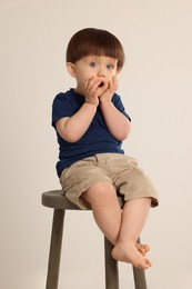 Photo of Emotional little boy sitting on stool against light grey background