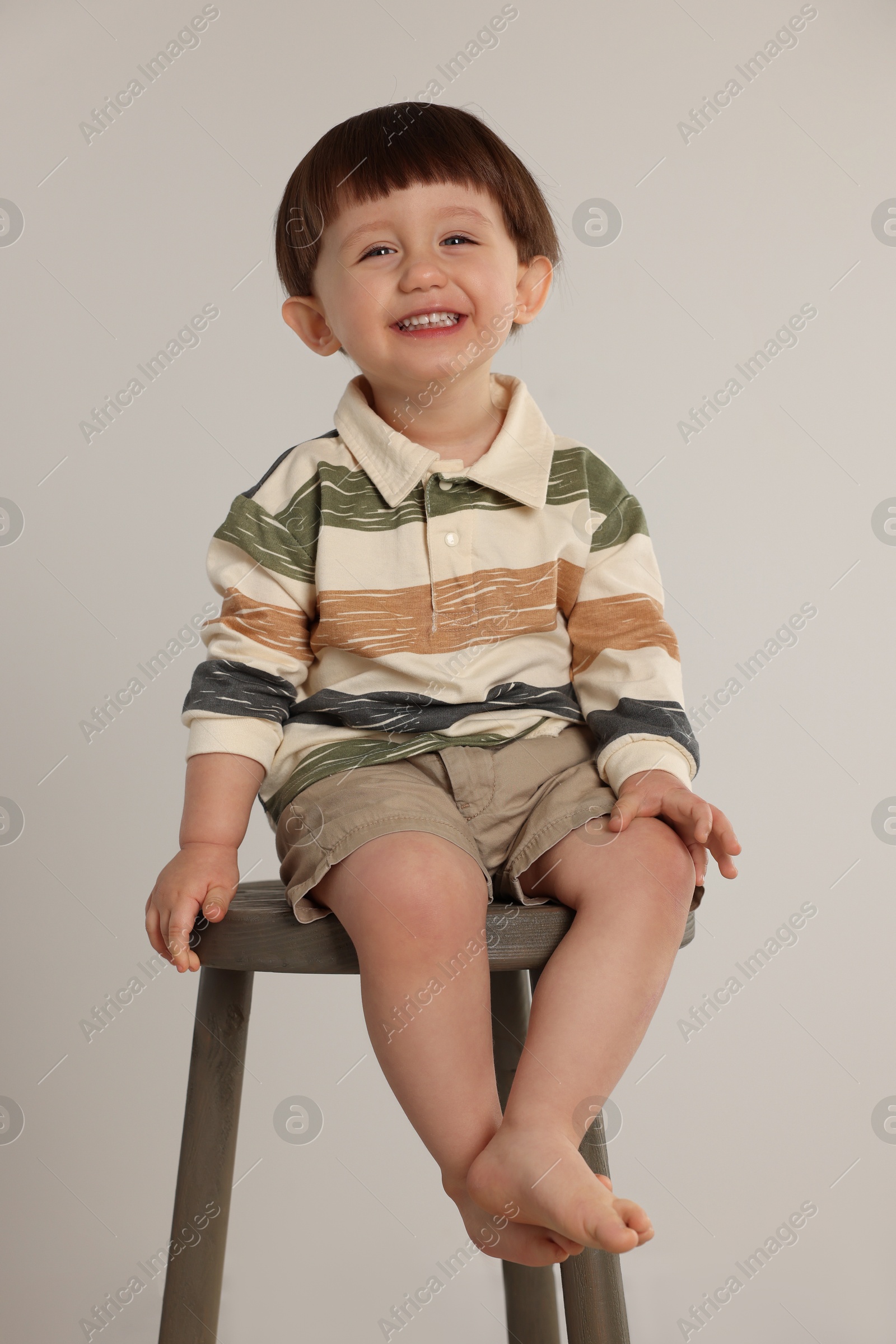 Photo of Happy little boy sitting on stool against light grey background