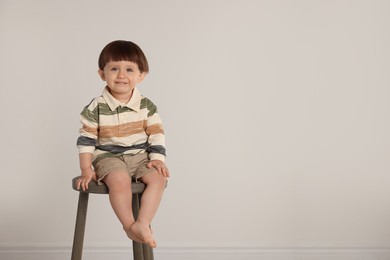 Photo of Happy little boy sitting on stool against light grey background. Space for text