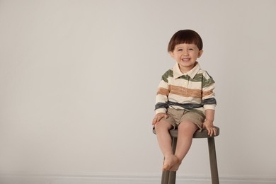 Photo of Happy little boy sitting on stool against light grey background. Space for text