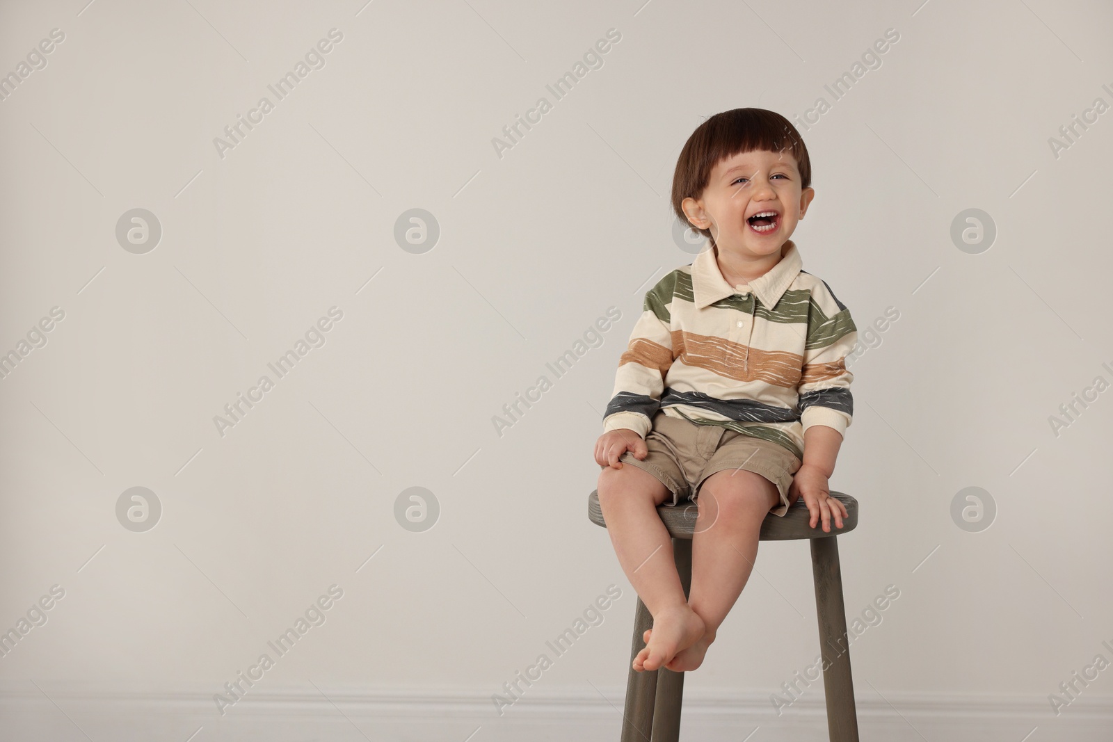 Photo of Emotional little boy sitting on stool against light grey background. Space for text