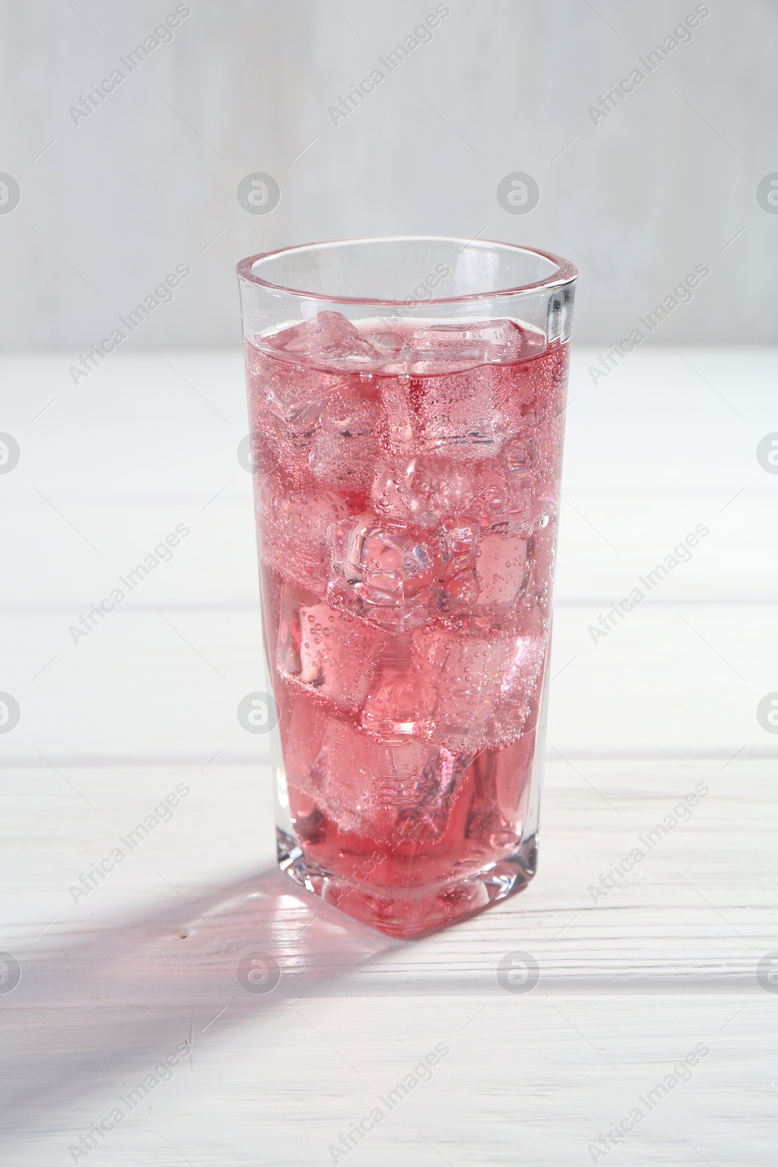 Photo of Sweet soda water with ice cubes in glass on white wooden table, closeup