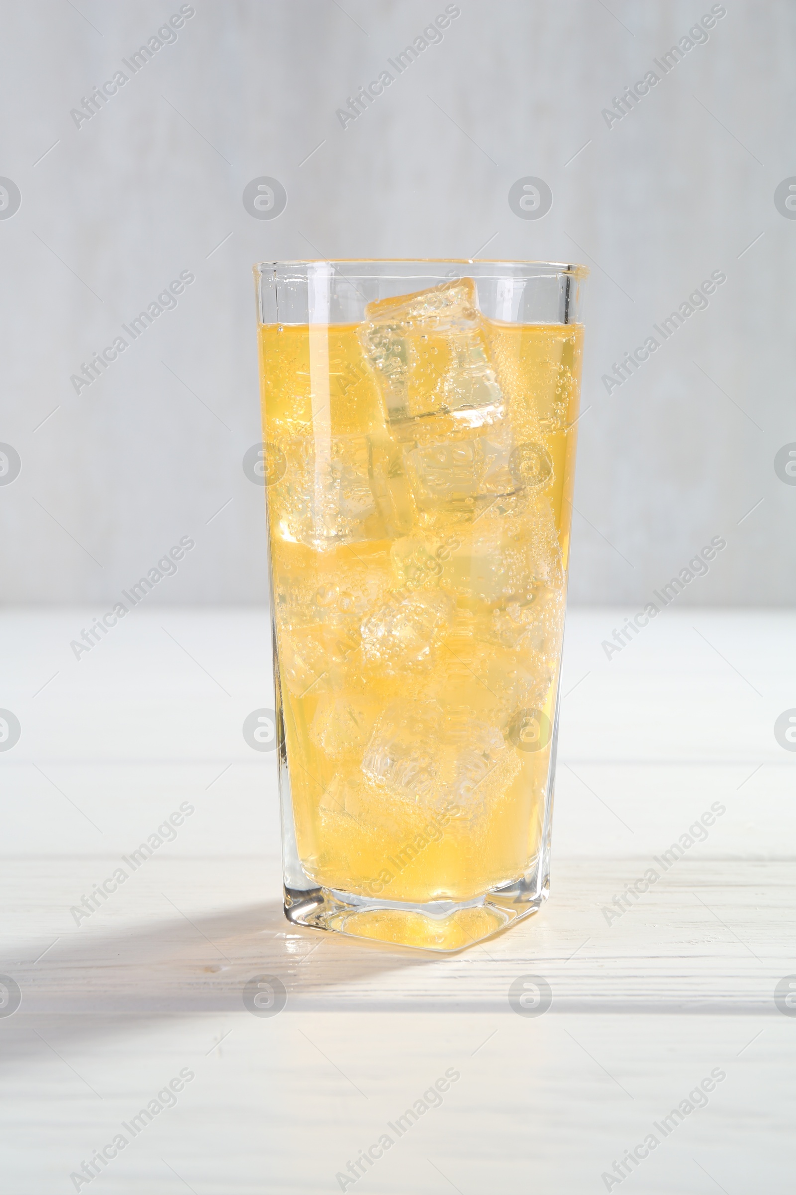 Photo of Sweet soda water with ice cubes in glass on white wooden table