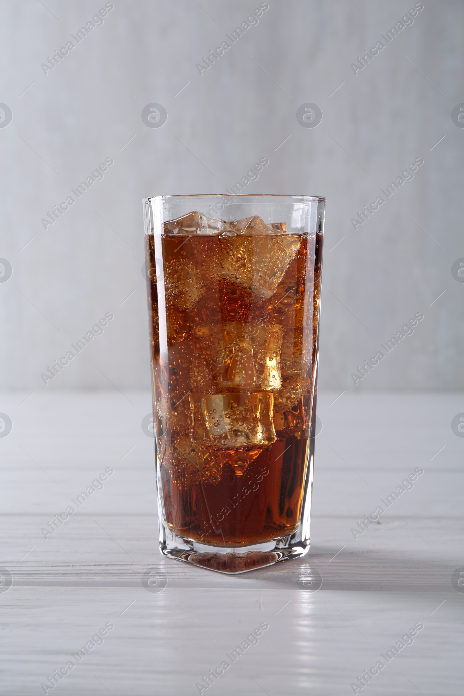 Photo of Sweet soda water with ice cubes in glass on white wooden table