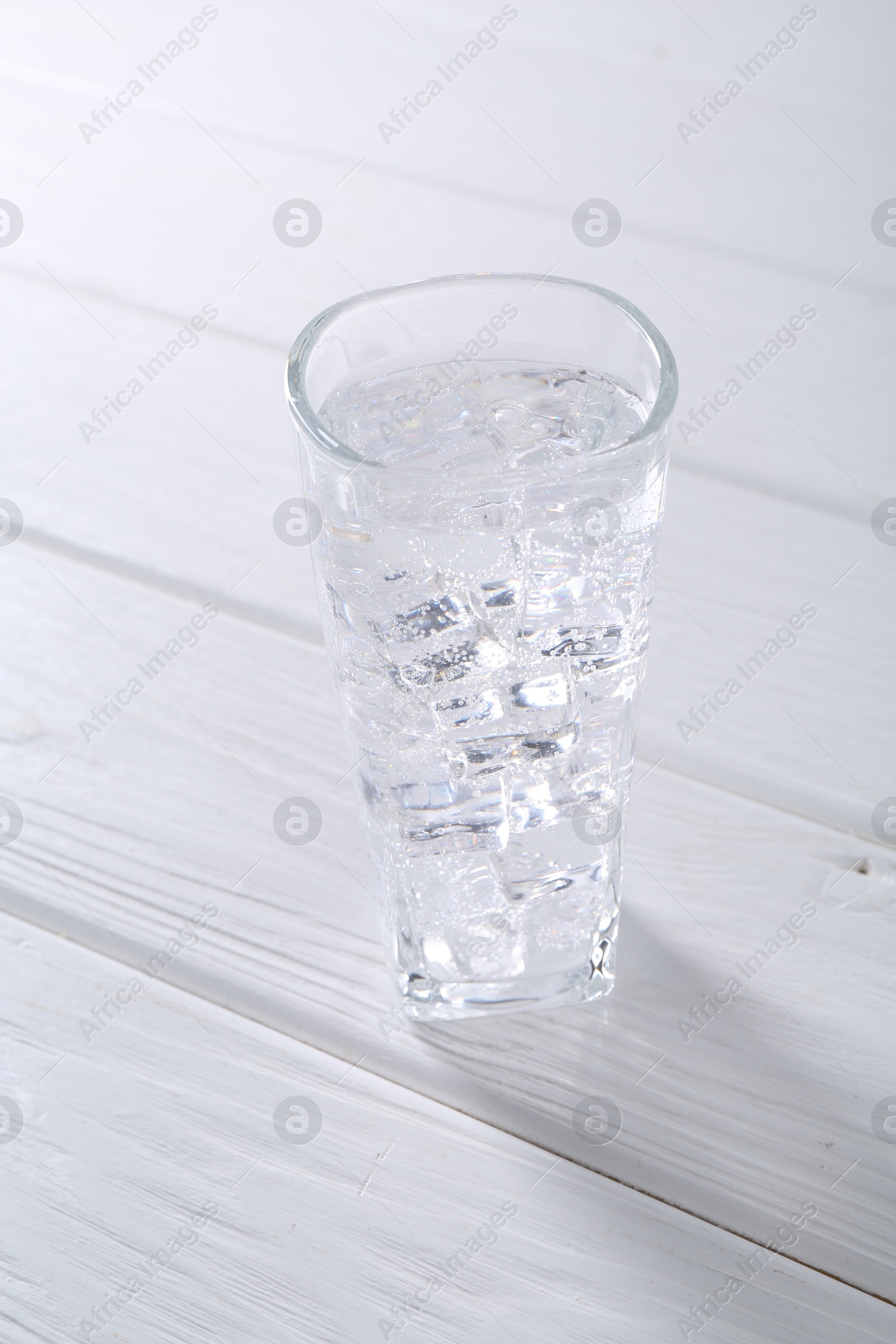 Photo of Refreshing soda water with ice cubes in glass on white wooden table, closeup