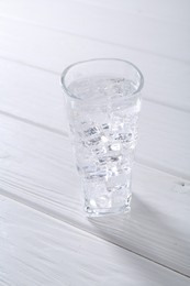 Photo of Refreshing soda water with ice cubes in glass on white wooden table, closeup