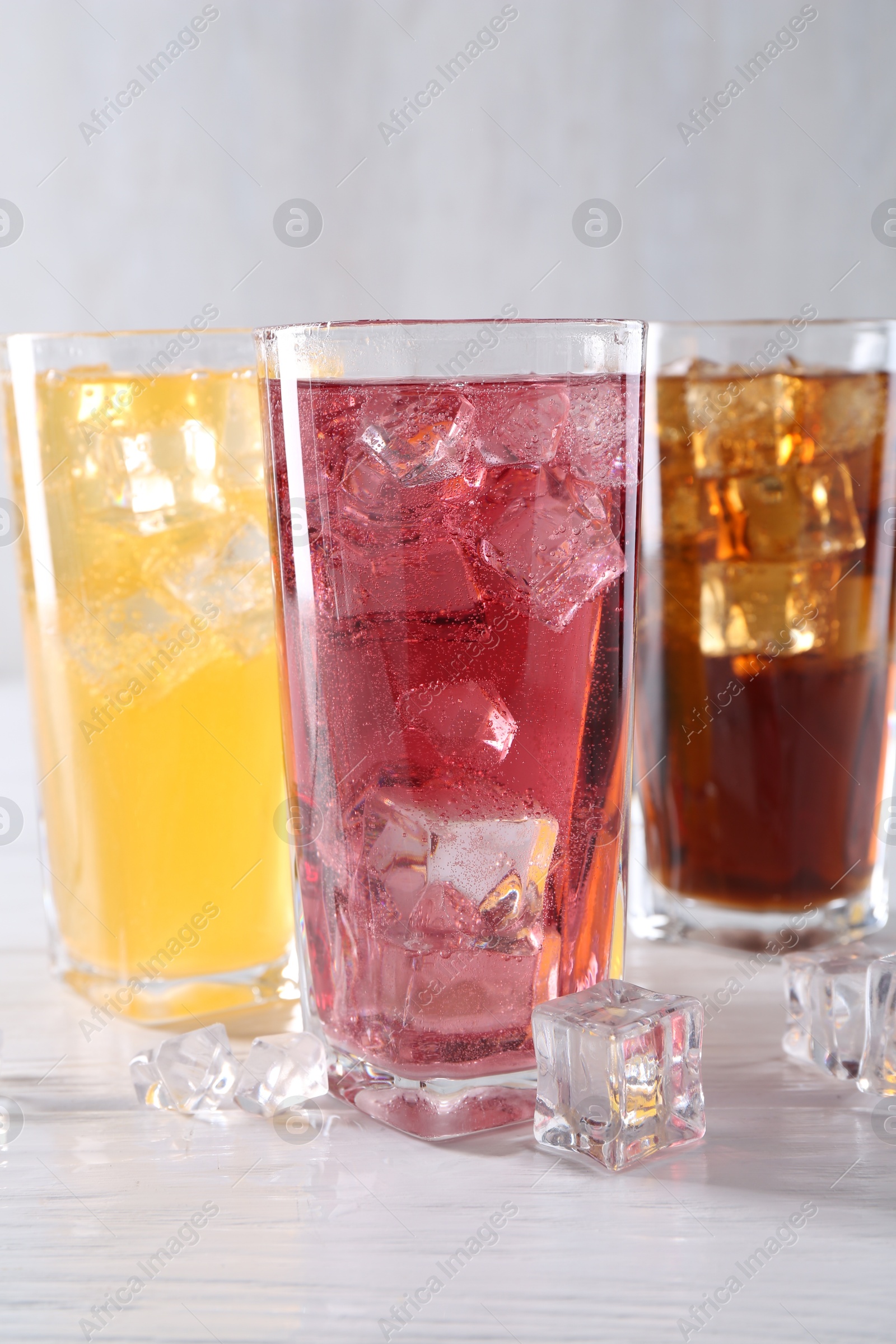 Photo of Soda water of different flavors in glasses with ice cubes on white wooden table