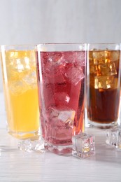 Photo of Soda water of different flavors in glasses with ice cubes on white wooden table