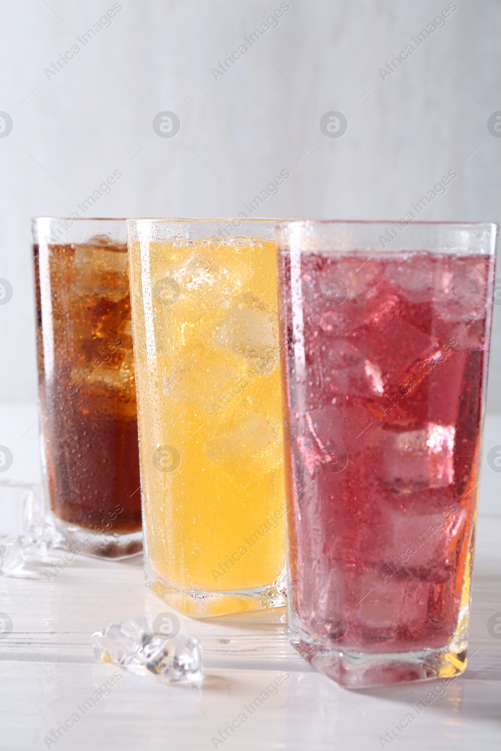 Photo of Soda water of different flavors in glasses with ice cubes on white wooden table, closeup