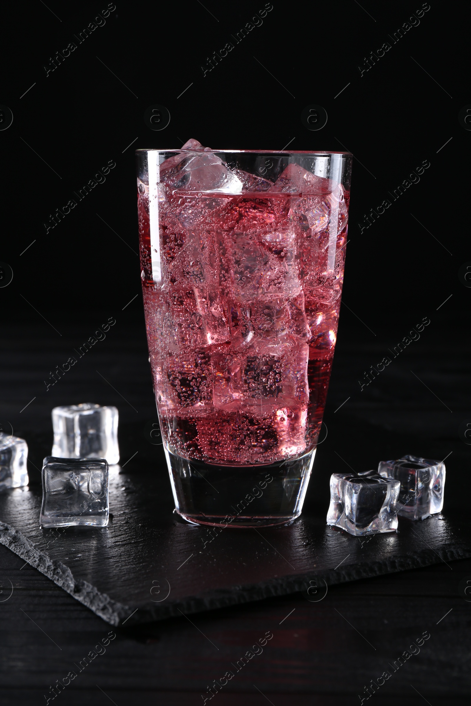 Photo of Sweet soda water in glass with ice cubes on black wooden table, closeup