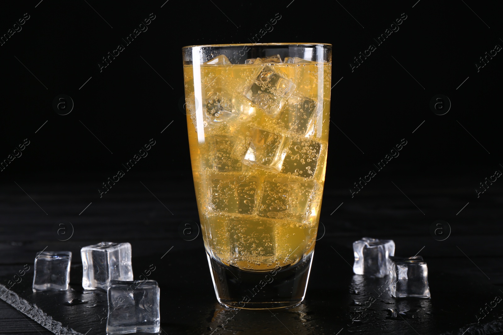 Photo of Sweet soda water in glass with ice cubes on black wooden table