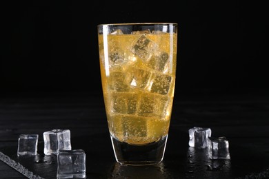 Photo of Sweet soda water in glass with ice cubes on black wooden table