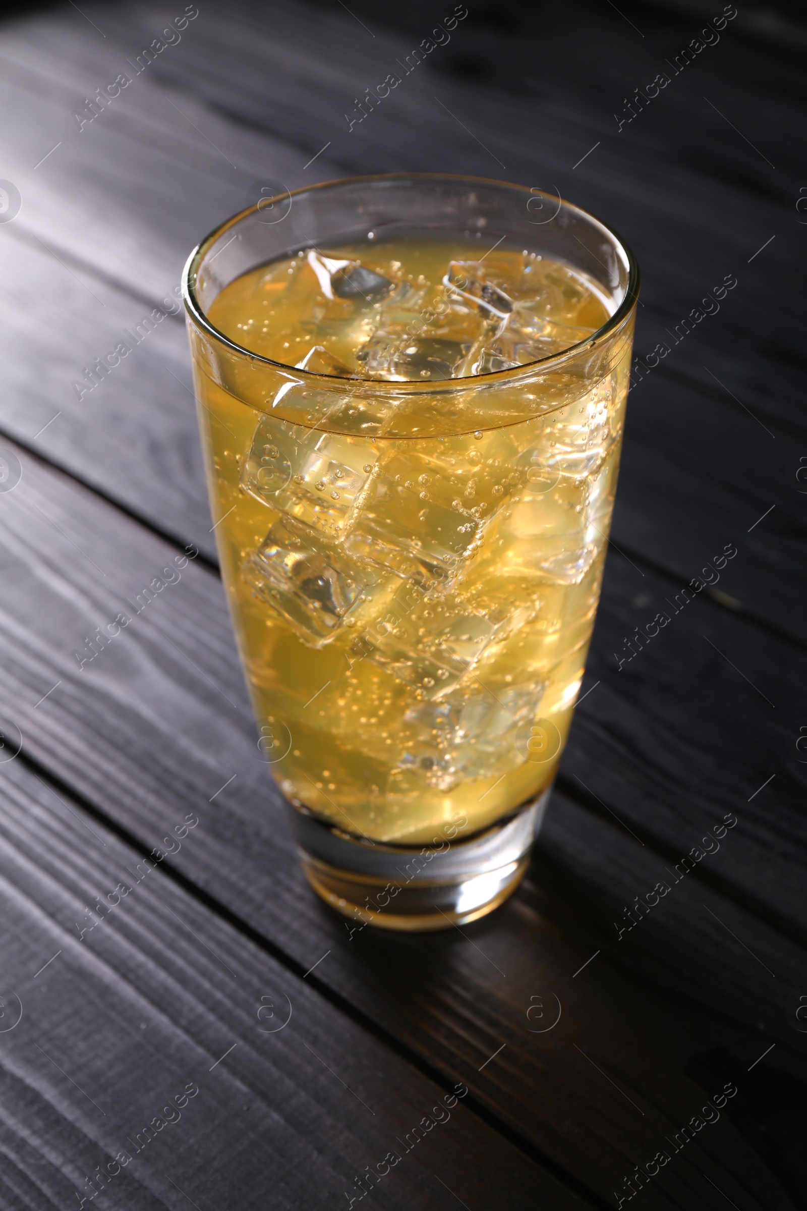 Photo of Sweet soda water with ice cubes in glass on black wooden table, closeup